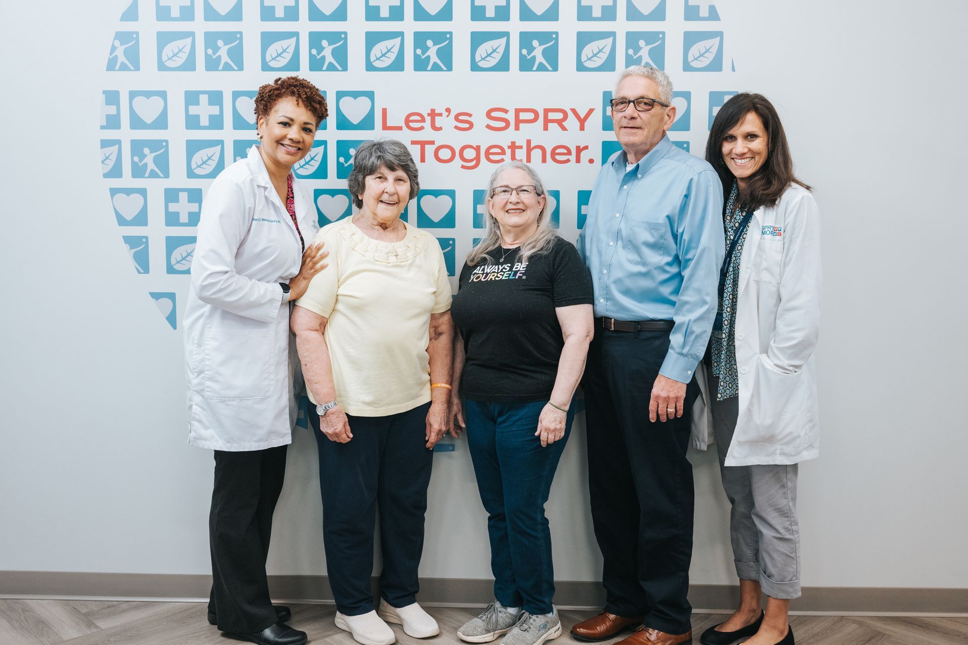 Five smiling people stand in front of a wall with a