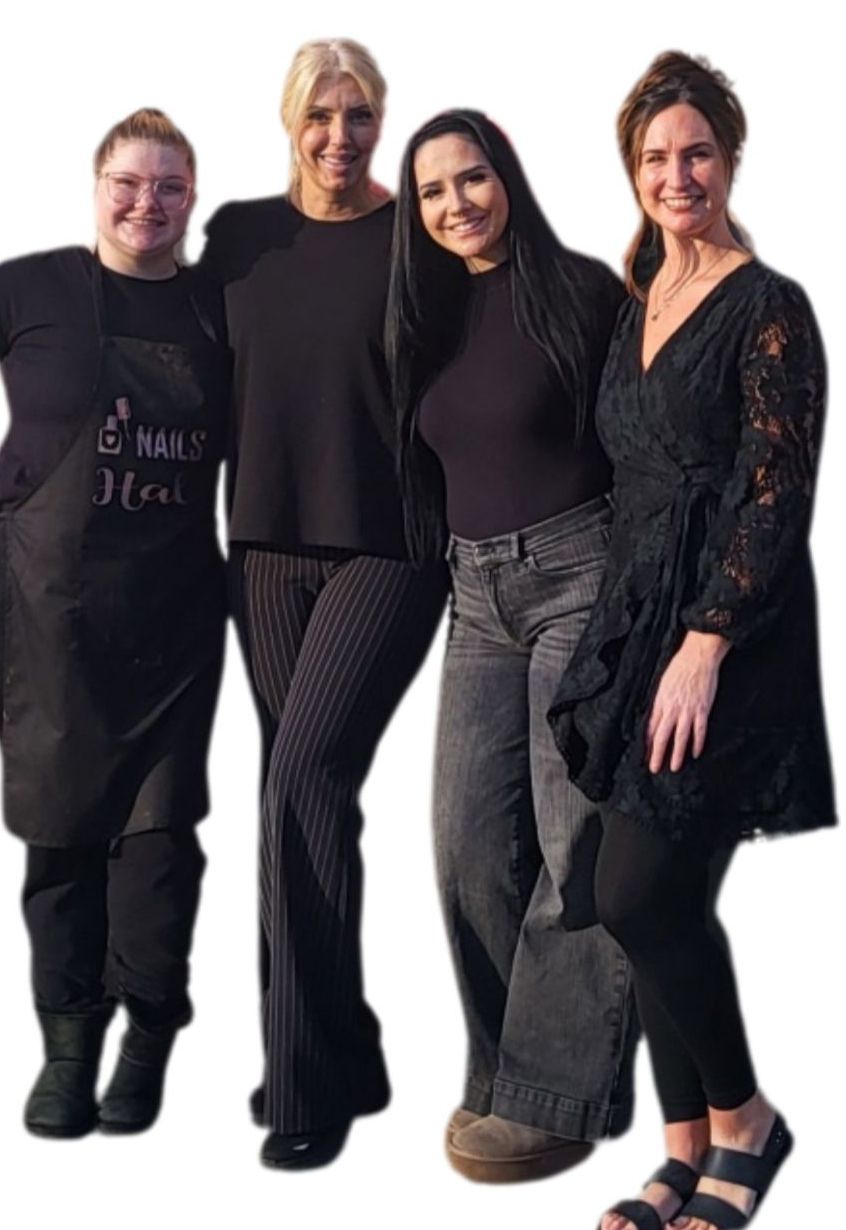 Four women stand together in a row against a white background, all smiling and wearing black clothing.