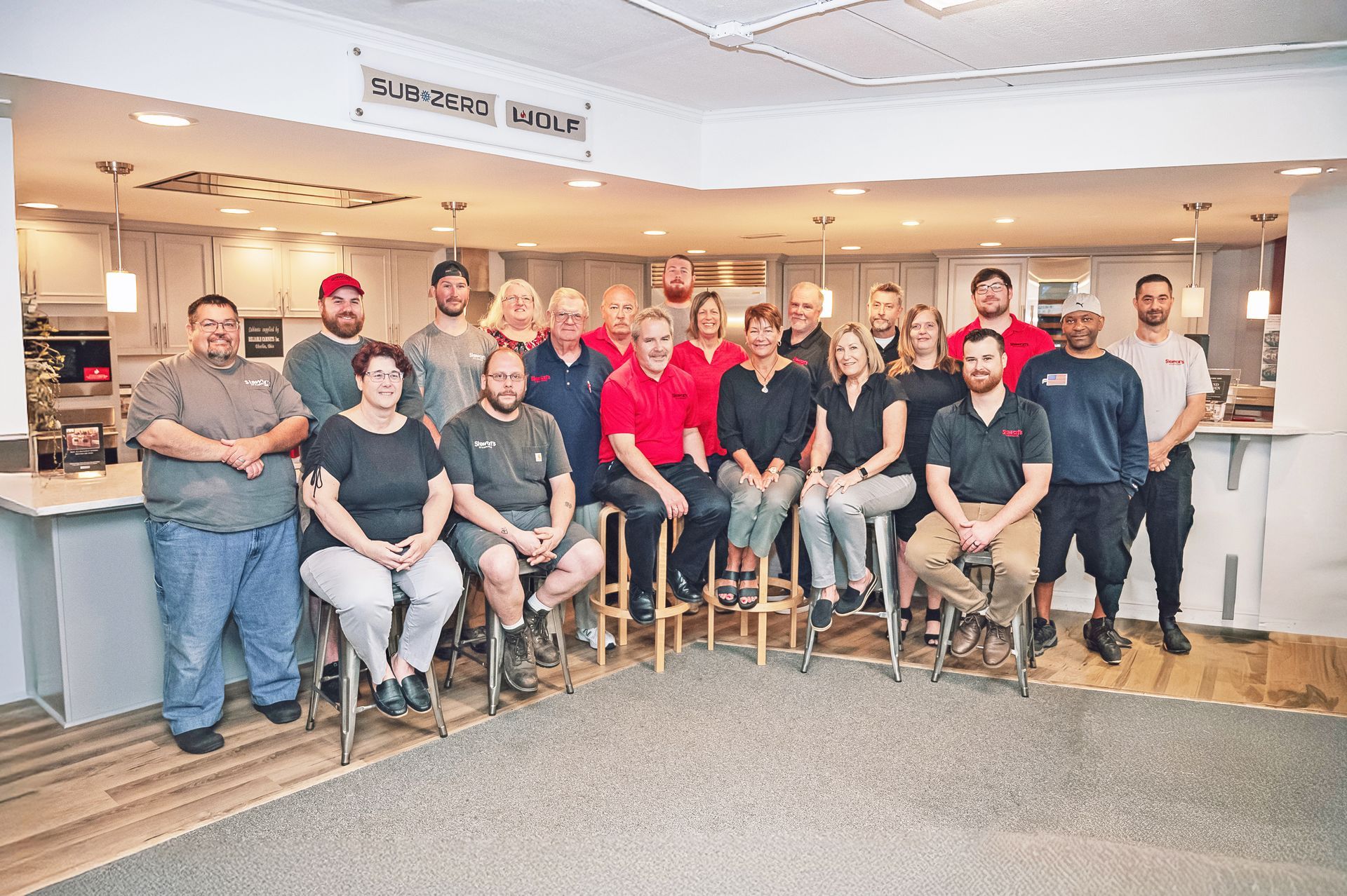 A group of employees stands and sits inside a showroom, posing for a photo in front of a modern kitchen display.
