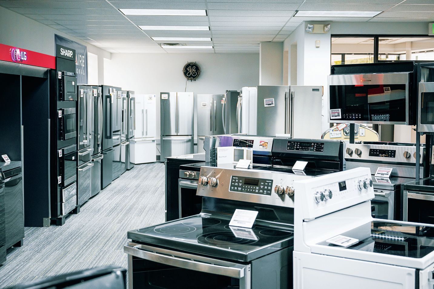 A well-lit appliance showroom featuring rows of stainless steel refrigerators and several stoves in the foreground.
