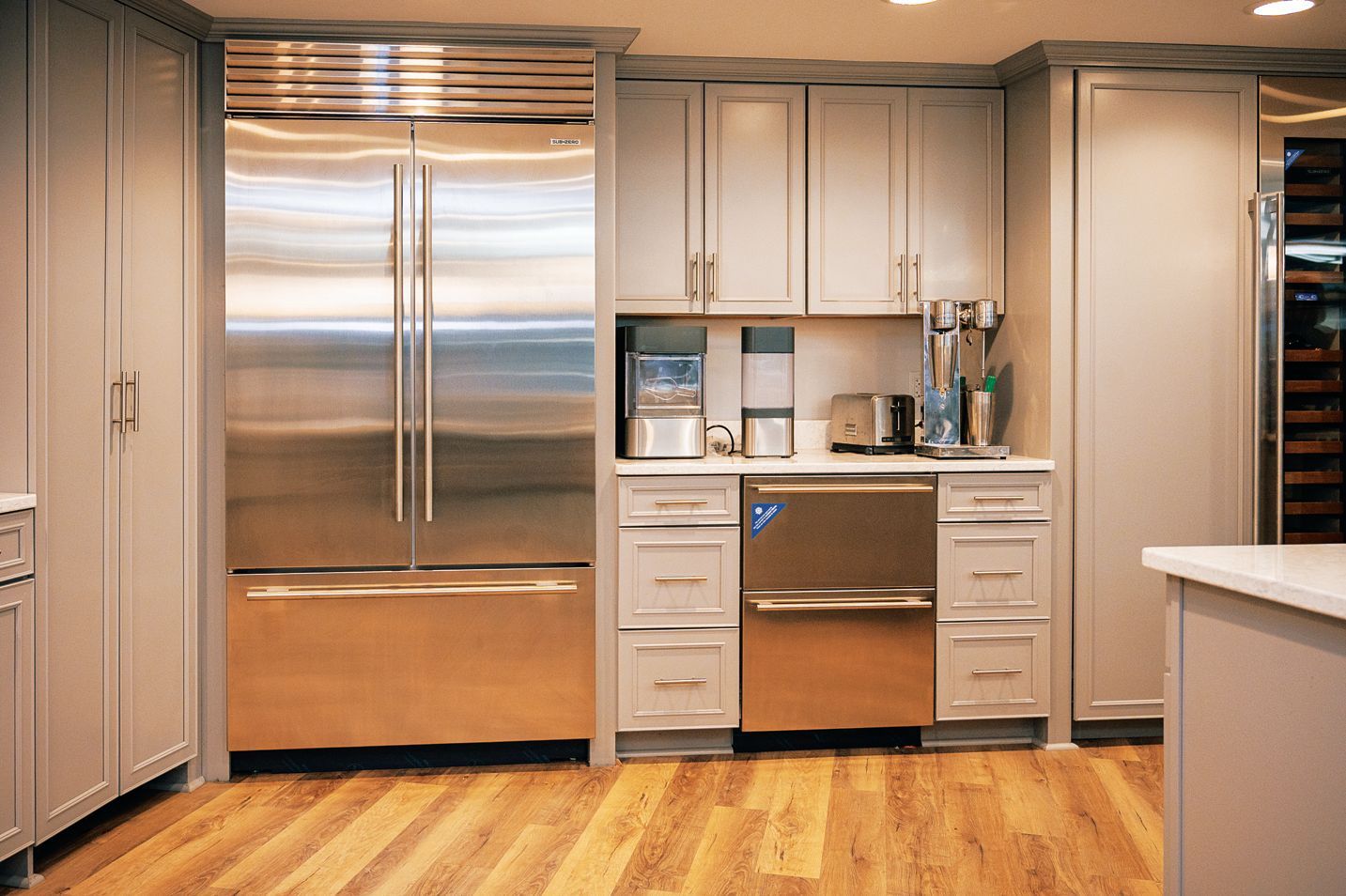 A modern kitchen featuring a stainless steel refrigerator, dishwasher, and cream-colored cabinets on hardwood floors.