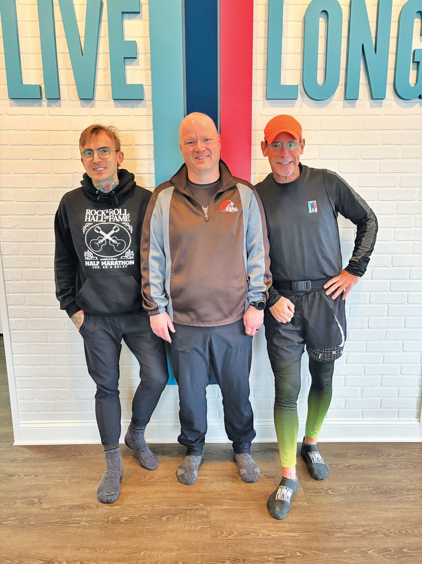Three people stand side-by-side against a white brick wall featuring the text