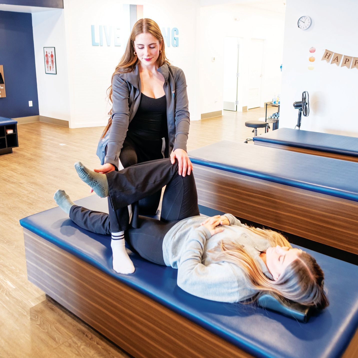 A practitioner performing a hip physical therapy stretch on a patient lying on a treatment table in a clinic.