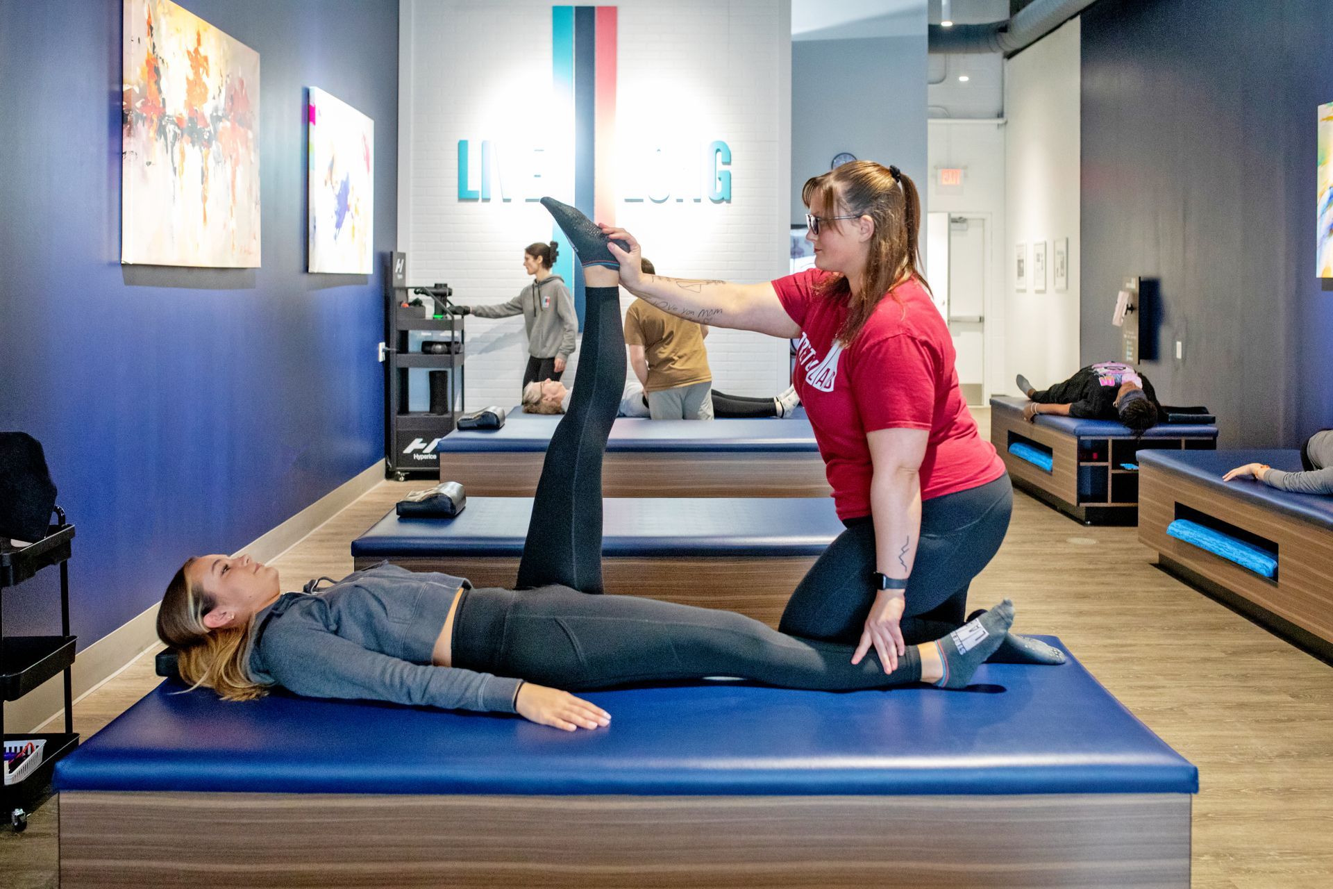 A practitioner performs a leg stretch on a client lying on a blue treatment table in a studio setting.