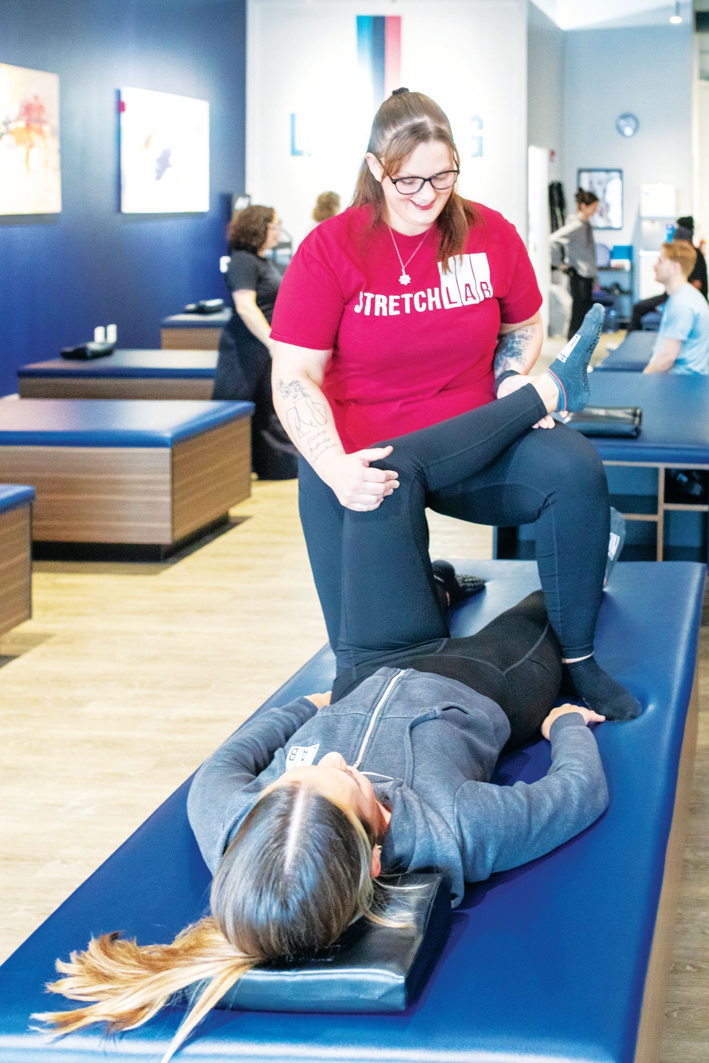 A professional stretches a person lying on a blue treatment table in a wellness center.