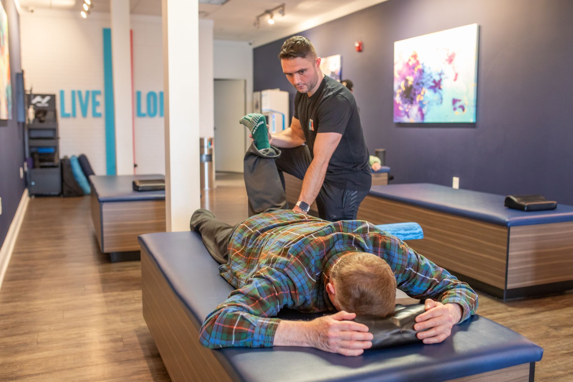 A therapist stretches the leg of a client lying face down on a professional massage table in a modern wellness studio.