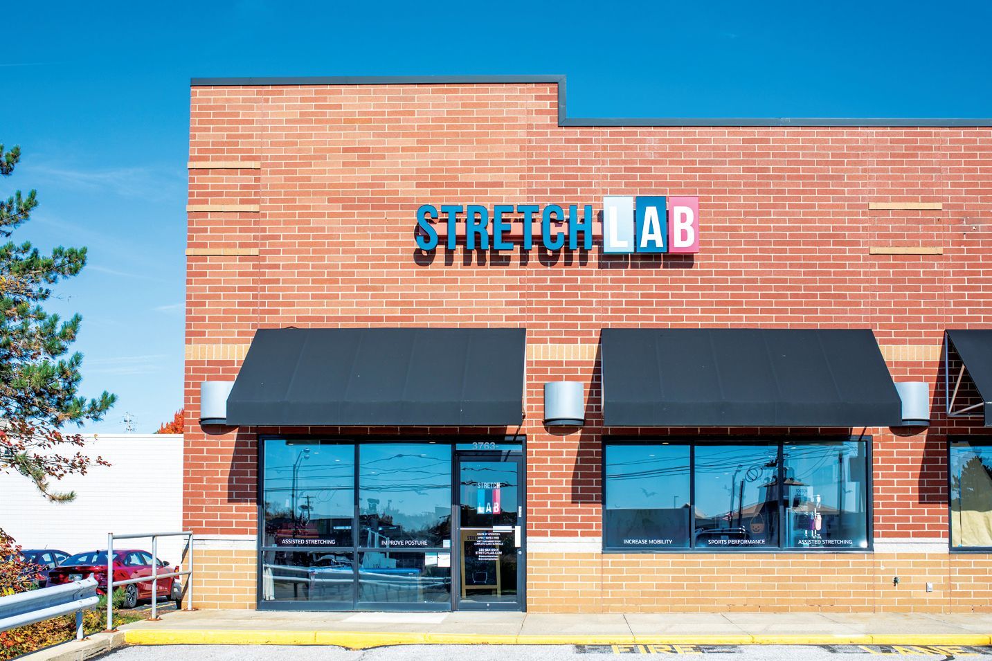 The storefront of a StretchLab business, featuring a brick facade, black awnings, and large glass windows.