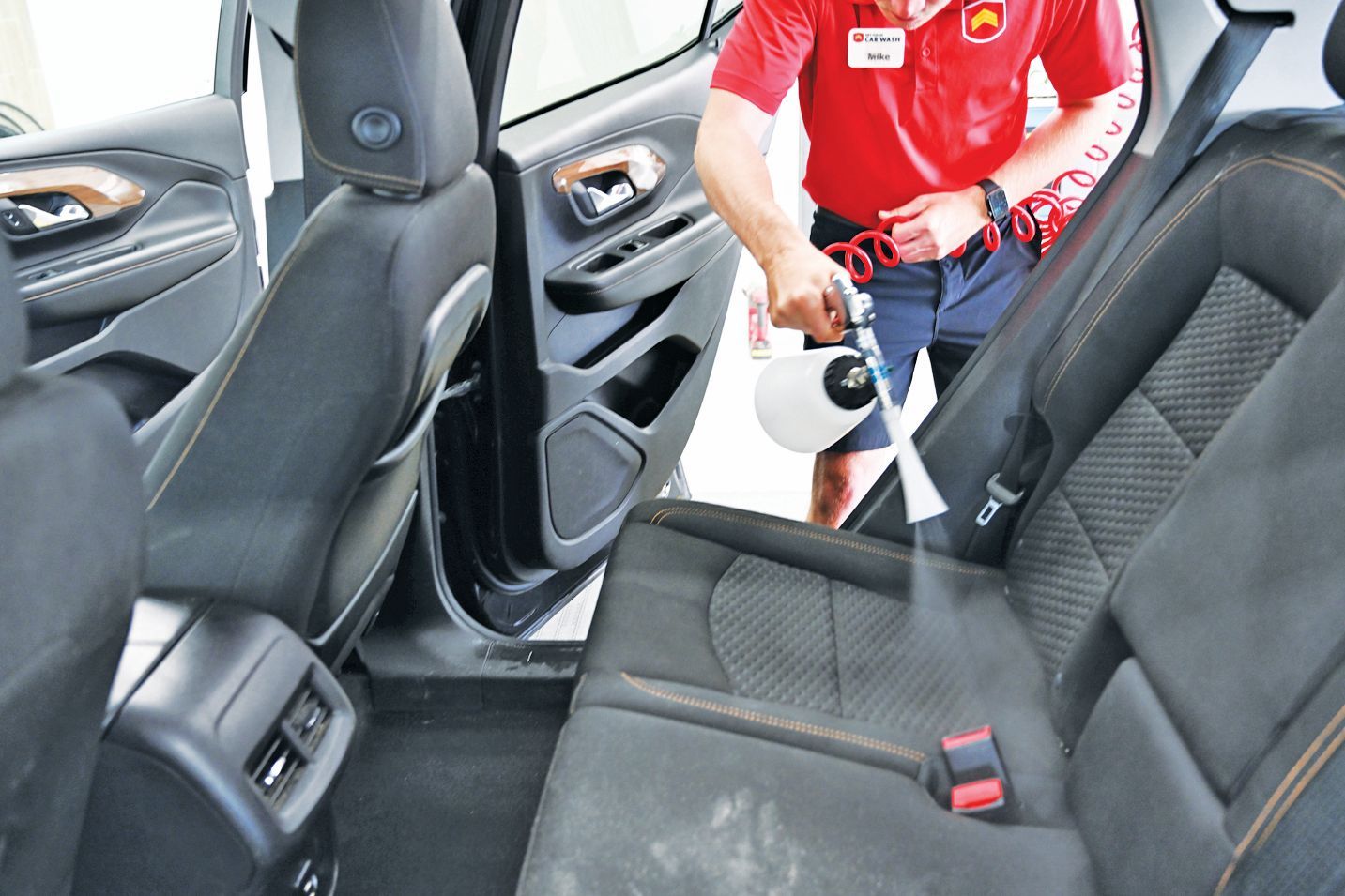 A professional cleaner uses a spray tool to clean the fabric back seat of a vehicle interior.