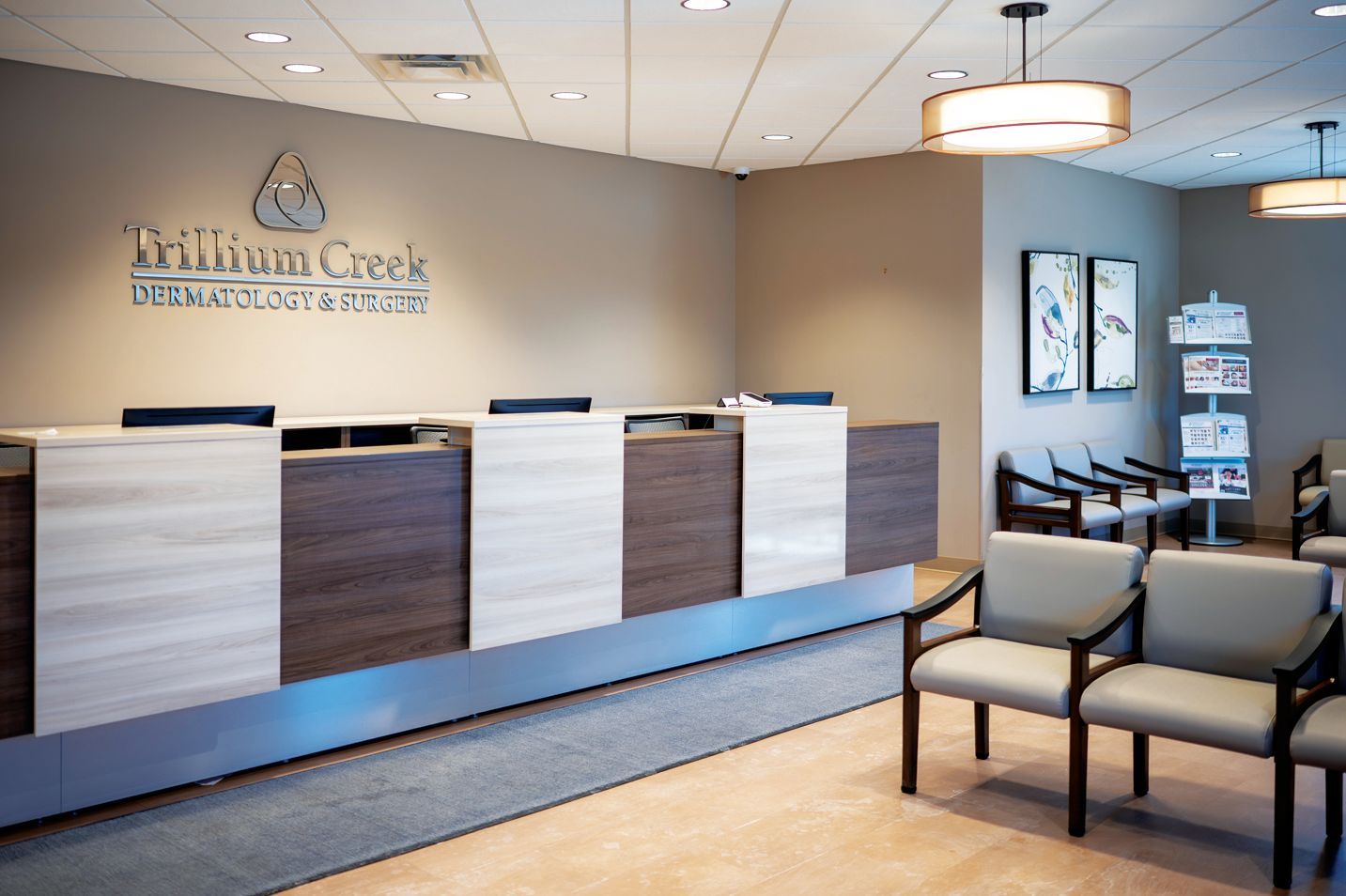 A reception desk with neutral tones, warm overhead lighting, and waiting area chairs in a professional medical office.