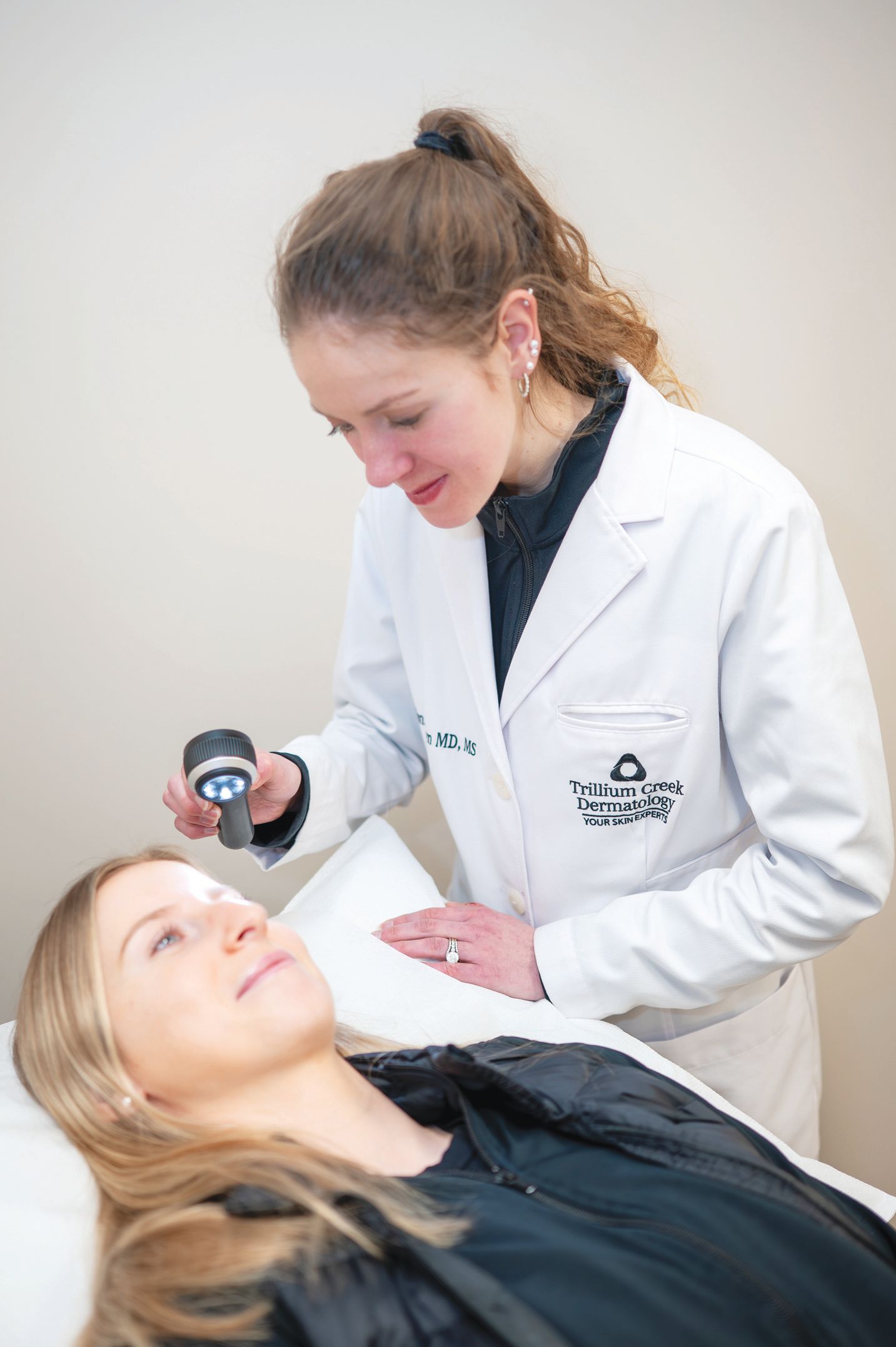 A professional examining a patient's skin using a dermatoscope in a clinical setting.