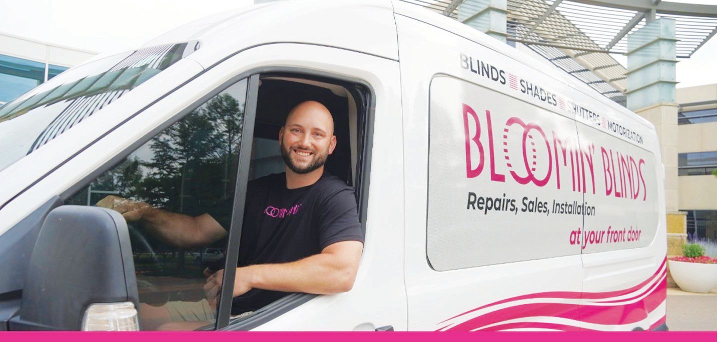 A smiling person in a black t-shirt sits in the driver's seat of a white van branded with 