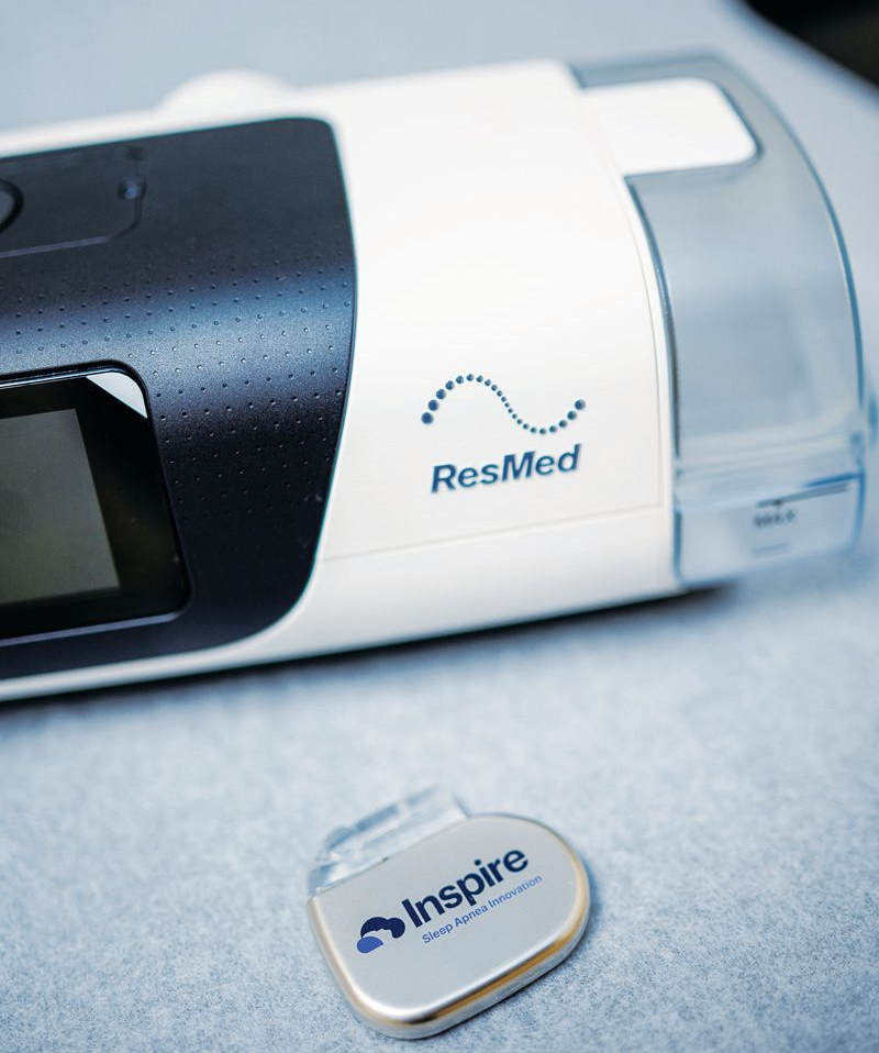 A ResMed CPAP machine sits behind an Inspire medical device, both displayed on a light surface.