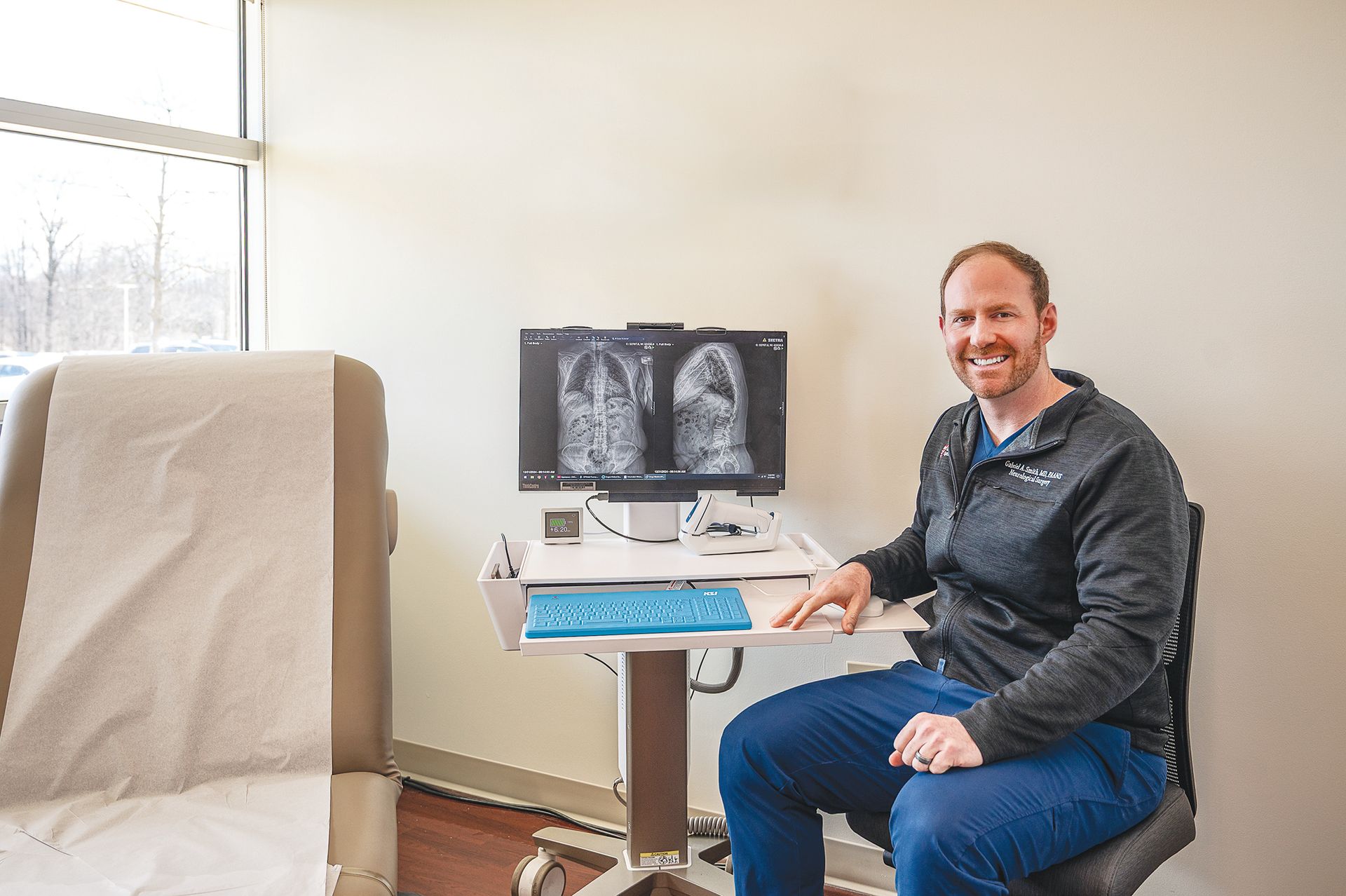 A medical professional sitting in an office next to a computer displaying diagnostic lung scans.