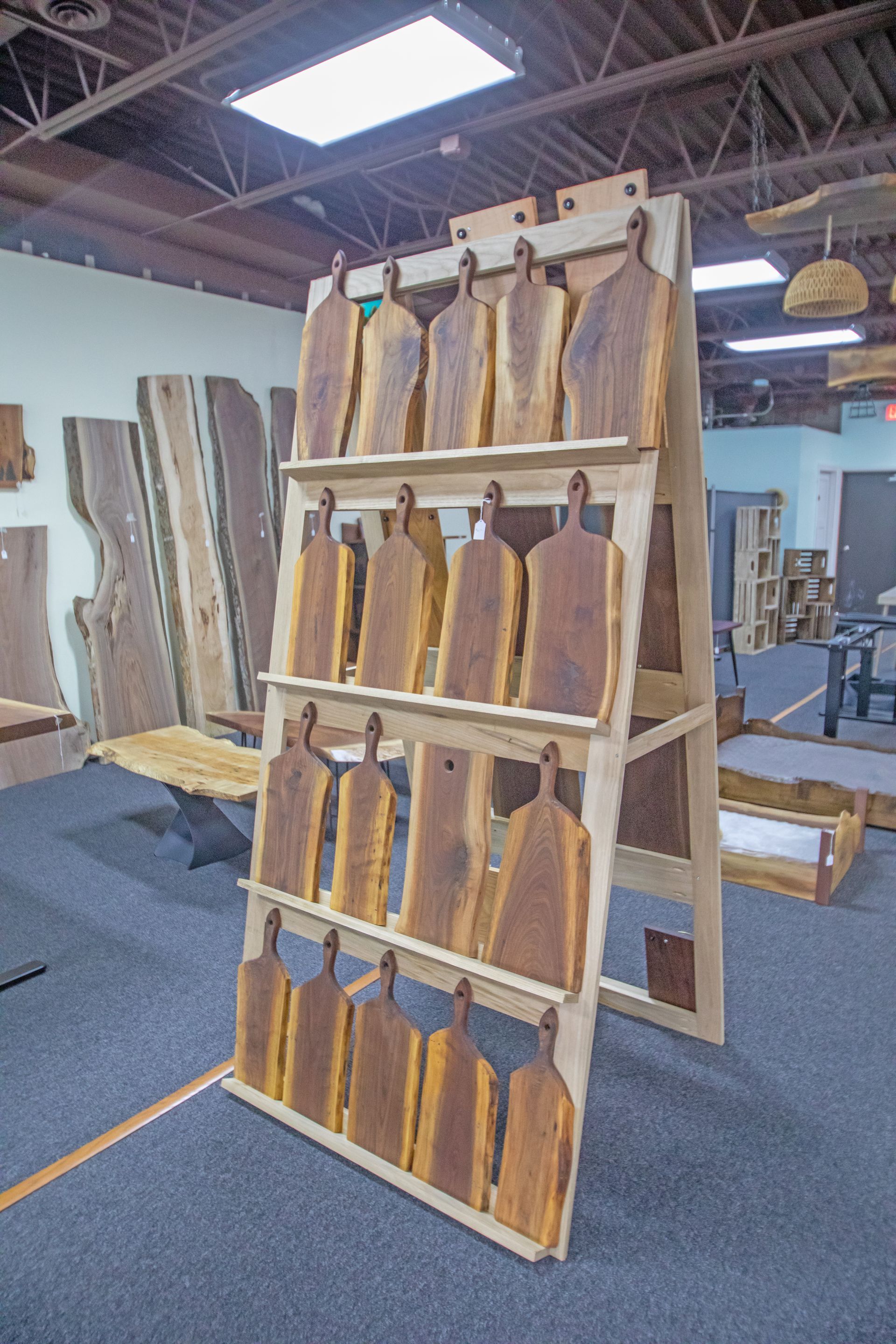 A wooden display rack holds rows of handcrafted live-edge wooden serving boards in a workshop or showroom.