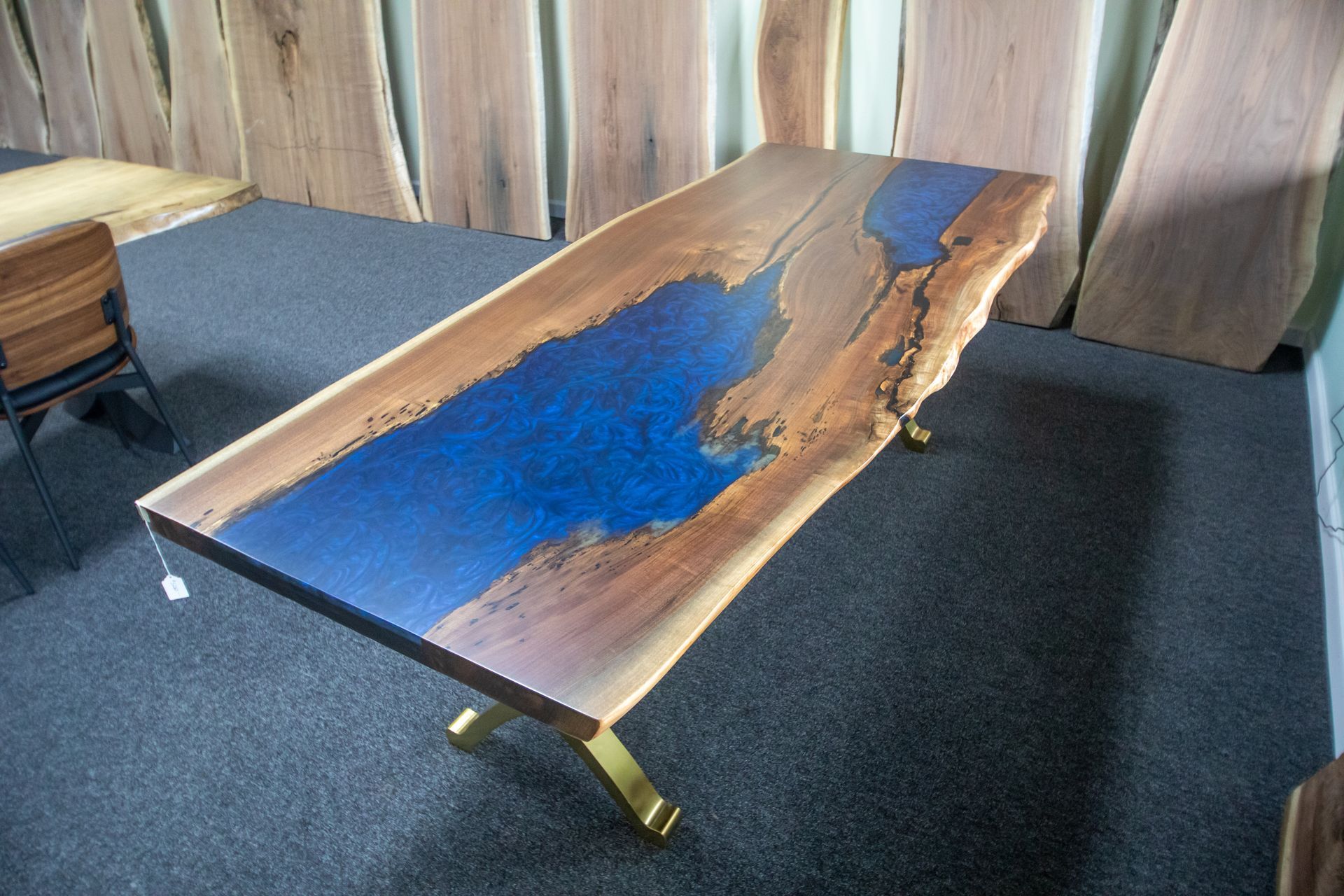 A live-edge wood dining table with a vibrant blue epoxy resin river insert and gold-colored metal legs in a showroom.