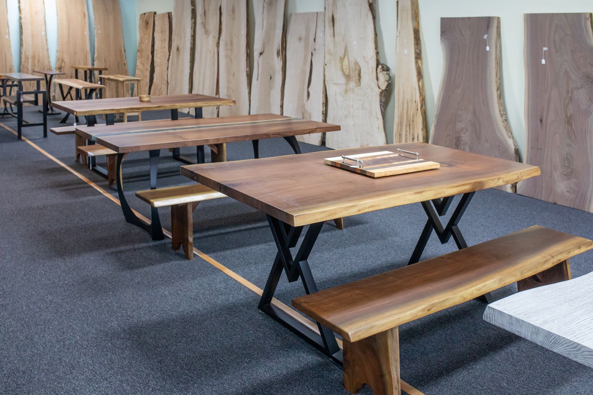 A showroom display featuring several wooden live-edge dining tables and matching benches with black metal X-shaped legs.
