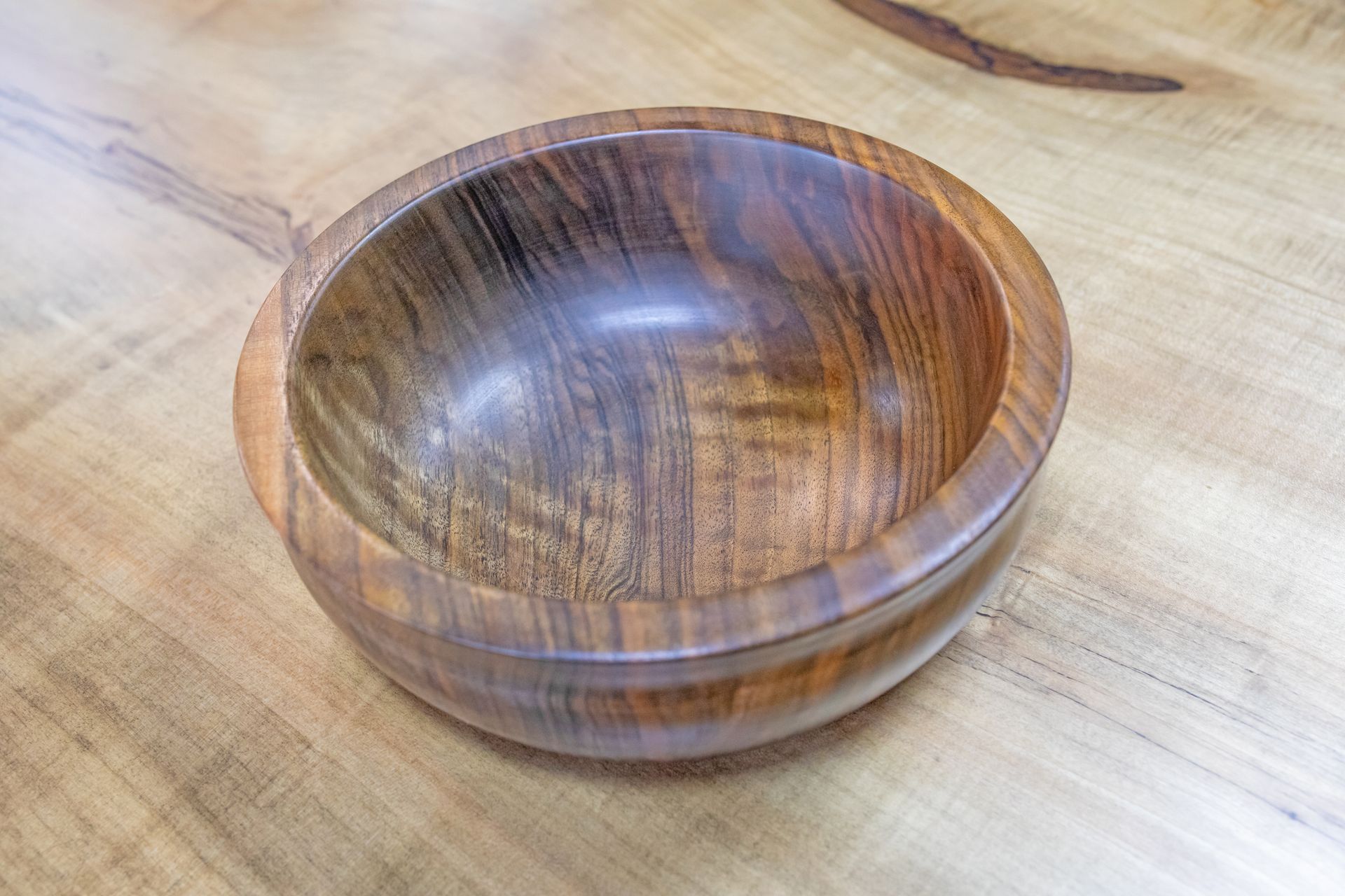 A smooth, circular wooden bowl with natural grain patterns sits centered on a light-colored wood surface.