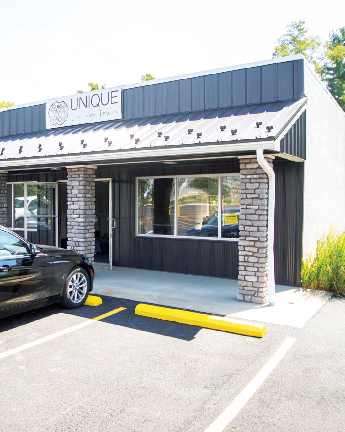 A modern commercial storefront with a black metal awning, stone-accented columns, and a parking space out front.