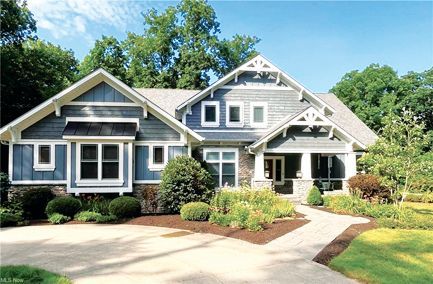 A two-story blue-gray shingled house with a stone base, white trim, gabled roofs, and a paved driveway.