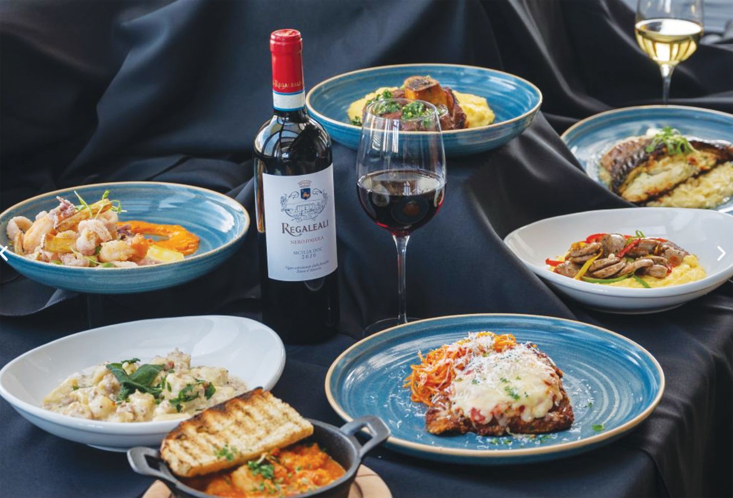 A spread of gourmet Italian dishes and wine arranged on a black tablecloth.