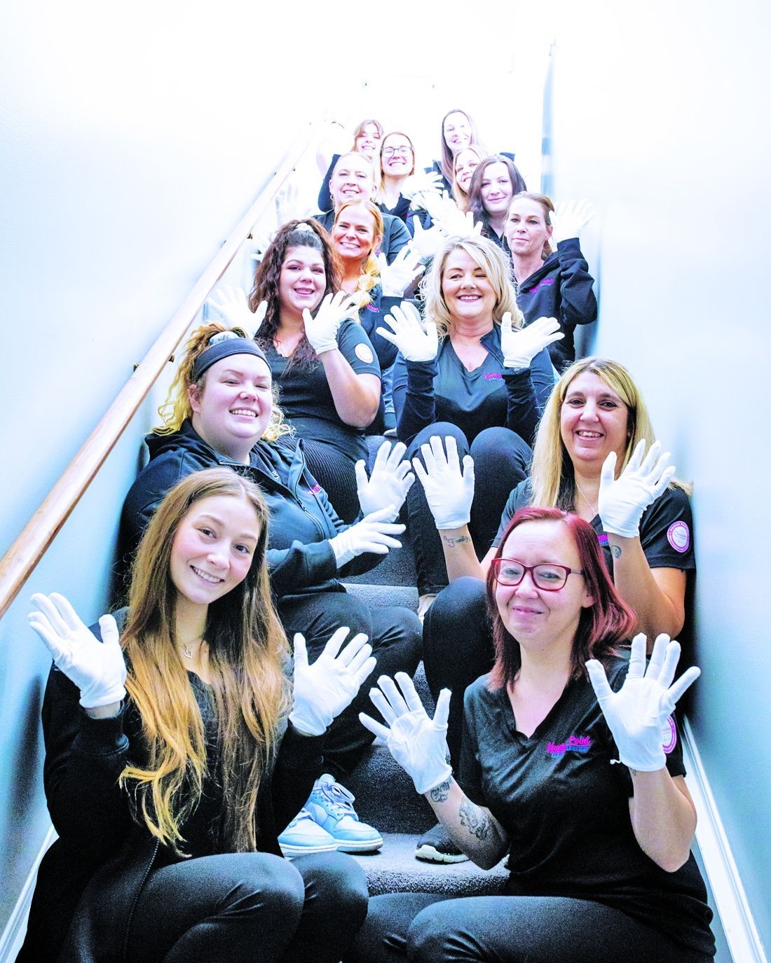 A group of people wearing black shirts and white gloves sitting on a staircase, posing with their hands raised.