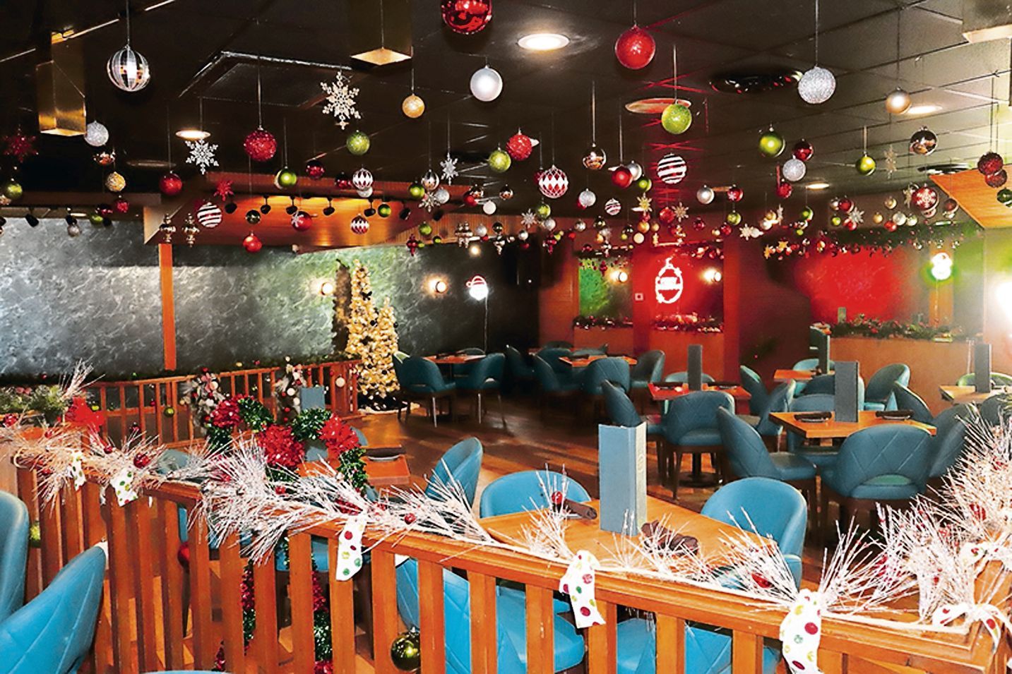 A restaurant dining area decorated with numerous Christmas ornaments hanging from the ceiling and white tinsel garlands.