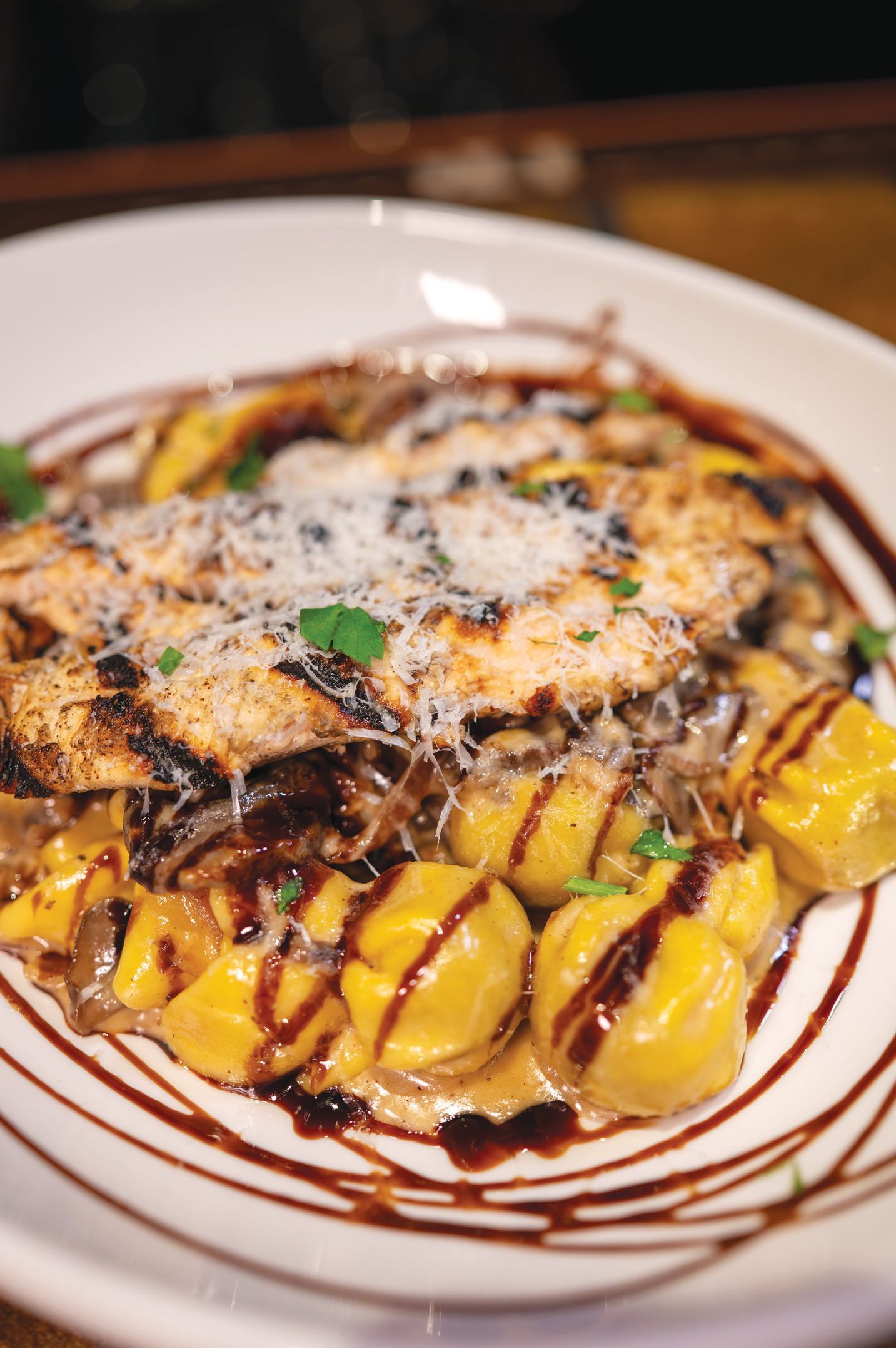 Grilled chicken breast served over yellow tortellini pasta, garnished with shredded cheese and a balsamic glaze drizzle.