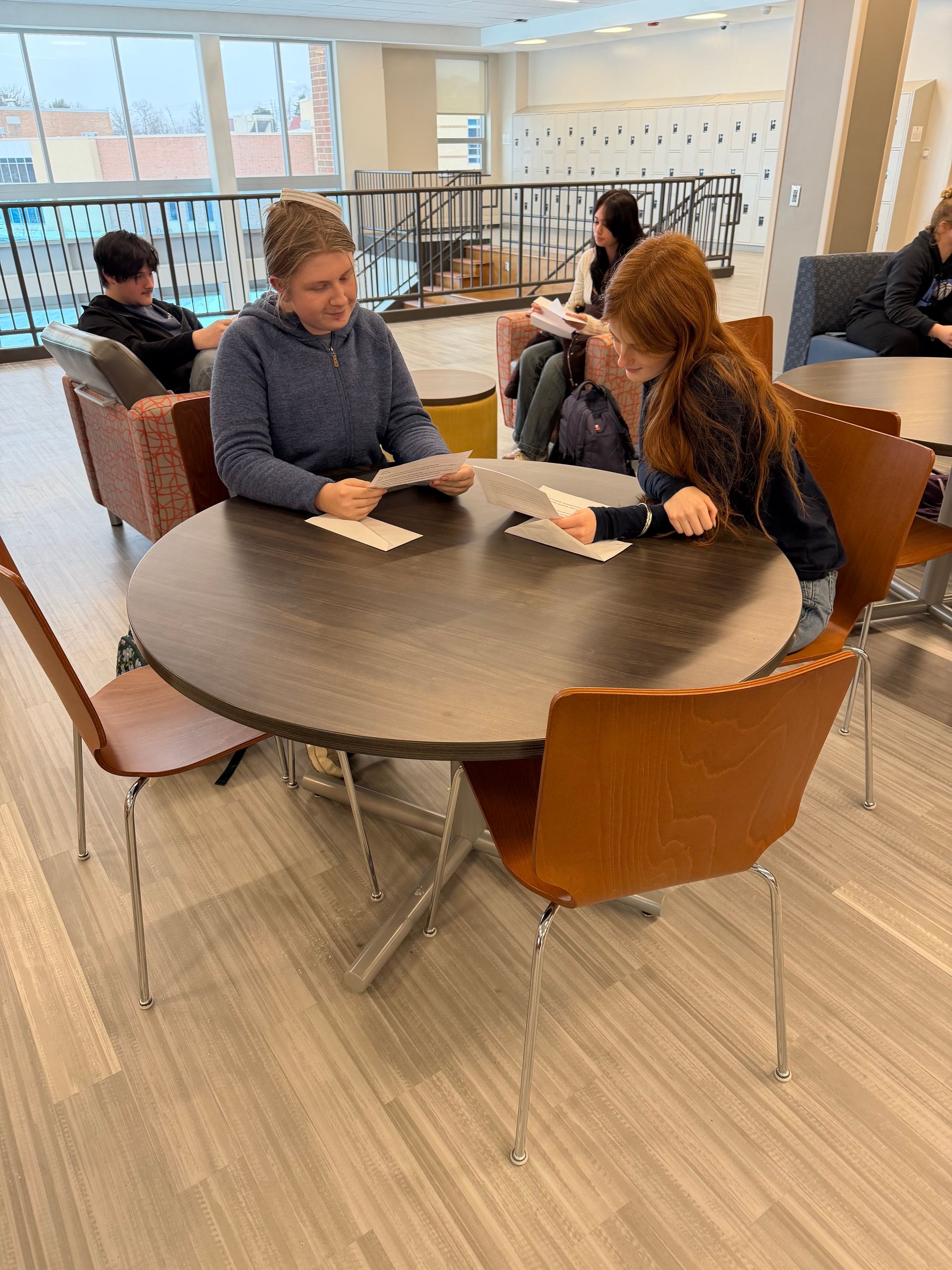 Two people seated at a circular table in a library space, reviewing papers together.