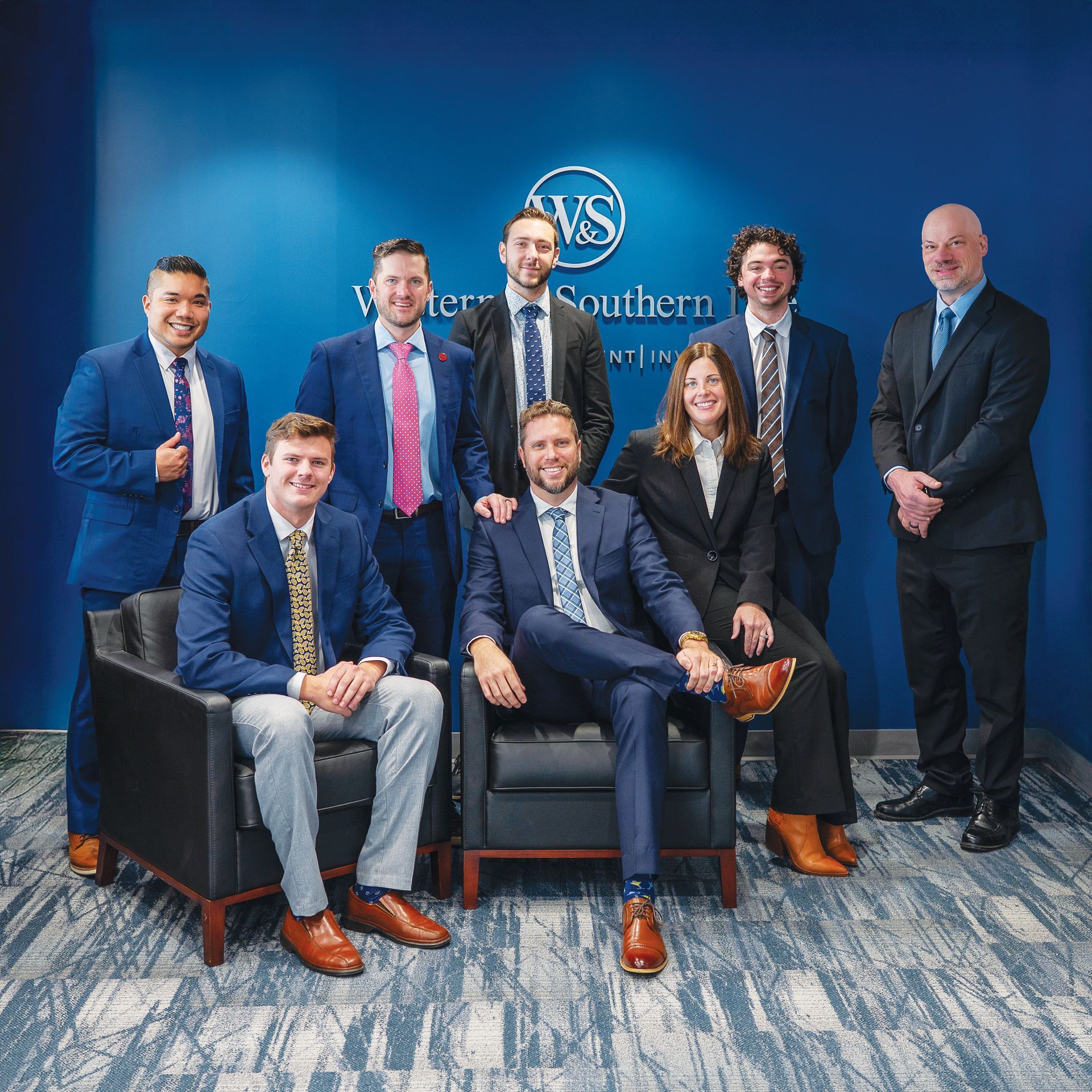 Group of seven professionals in business attire standing and sitting in front of a blue Western & Southern office wall.