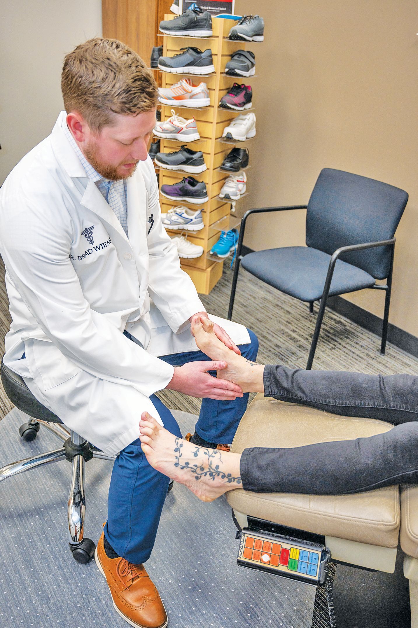 A healthcare provider in a lab coat examines a patient’s foot in a clinical office setting.