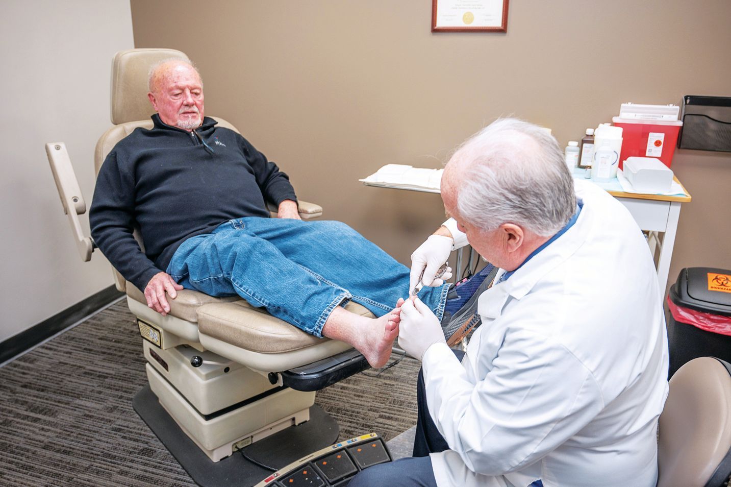 A medical professional wearing gloves examines a patient's foot in a clinical exam room.
