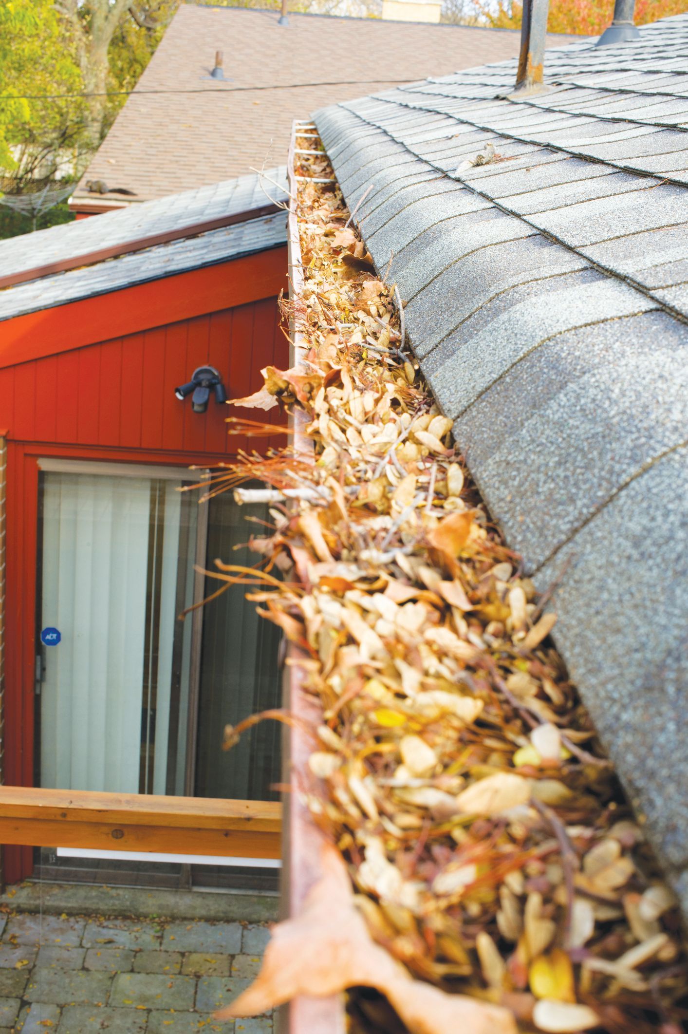 A residential roof gutter overflowing with dried brown leaves and debris.