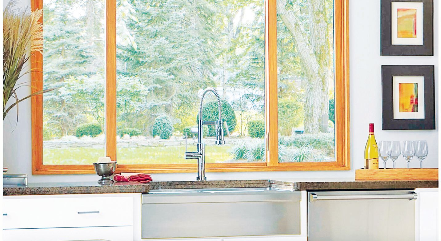 A kitchen sink area with a stainless steel apron front sink, modern faucet, and a large window looking onto a garden.