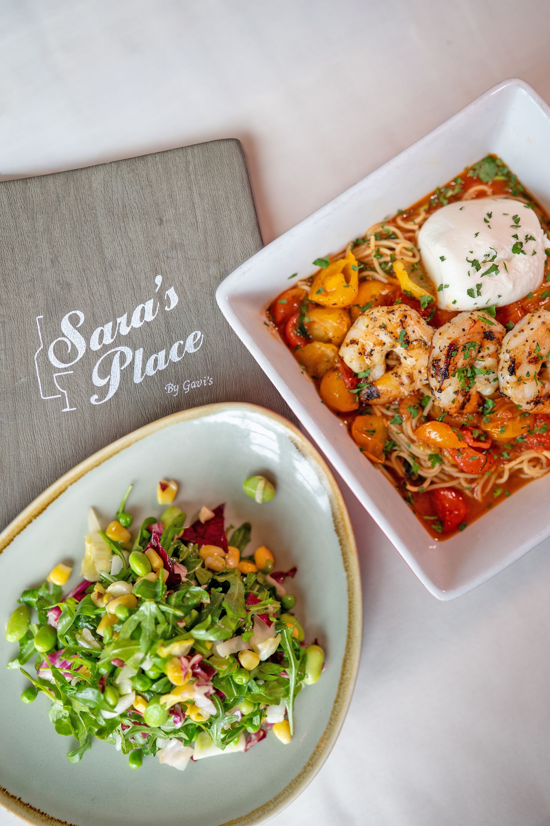 A top-down view of a salad, a shrimp pasta dish, and a menu branded