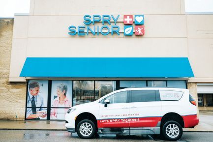 A white and red van parked in front of a Spry Senior building featuring medical and wellness-themed icons on the signage.