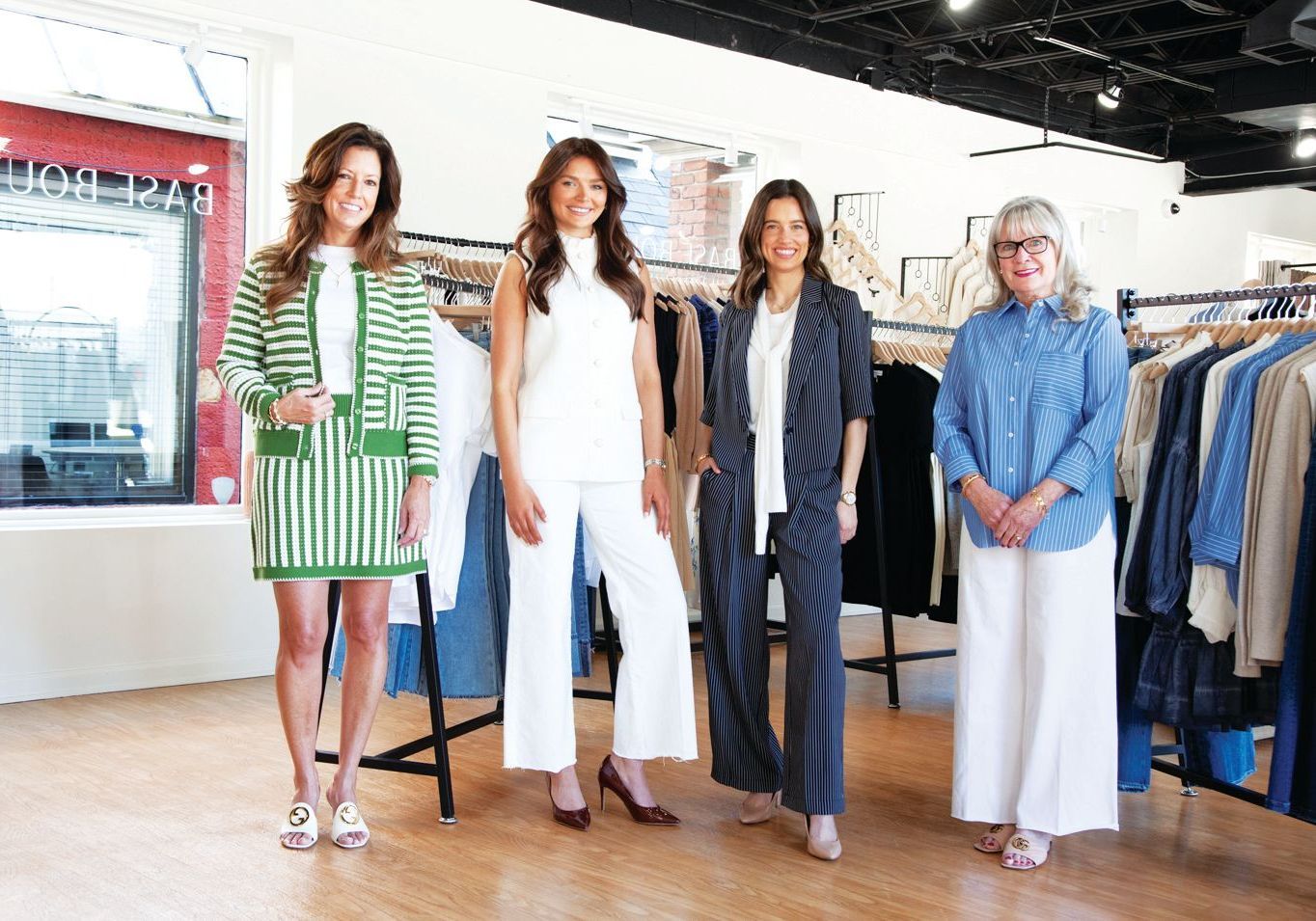 Four people pose together in a clothing boutique, wearing stylish outfits with racks of clothes in the background.