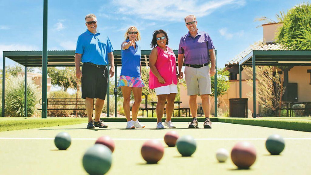 Four people smiling while playing bocce ball on an outdoor court with colorful balls and a white target ball.