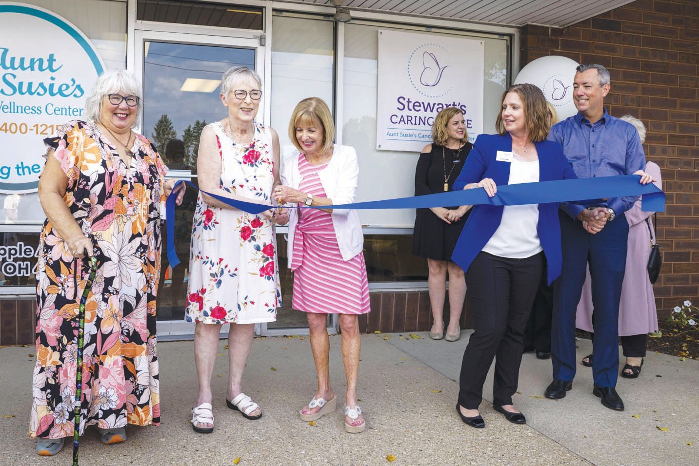 A group of people participate in a ribbon-cutting ceremony outside a building with signage for Aunt Susie's Cancer Care.