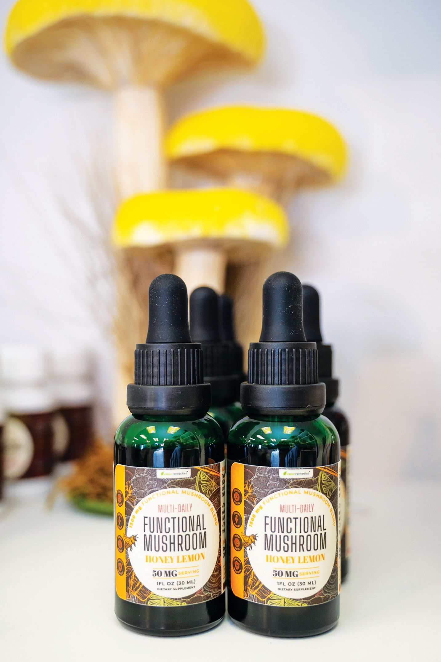 Two amber dropper bottles of mushroom tincture stand in front of decorative yellow mushroom ornaments.