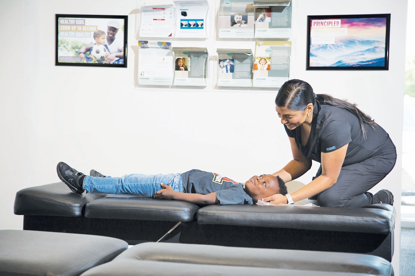 A professional in dark scrubs examines a patient lying on a treatment table in a clinical setting.