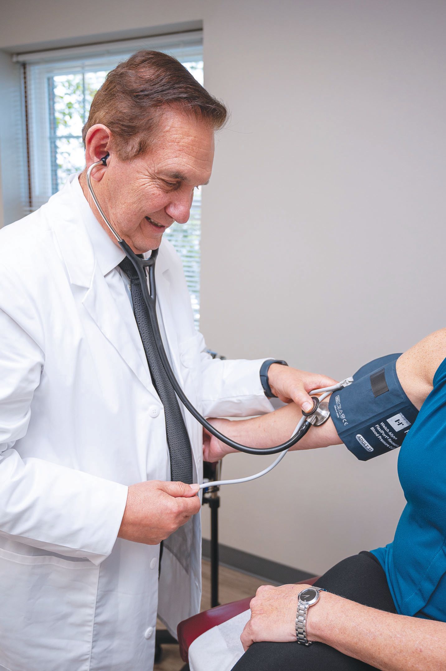 A medical professional in a white coat using a stethoscope to check a patient's blood pressure in an office.