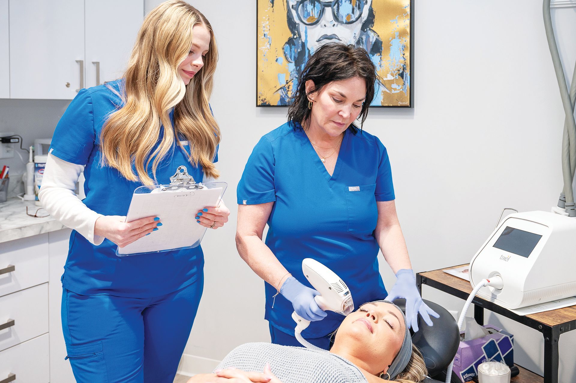 Medical professionals in blue scrubs perform a laser skin treatment on a patient in a clinical setting.