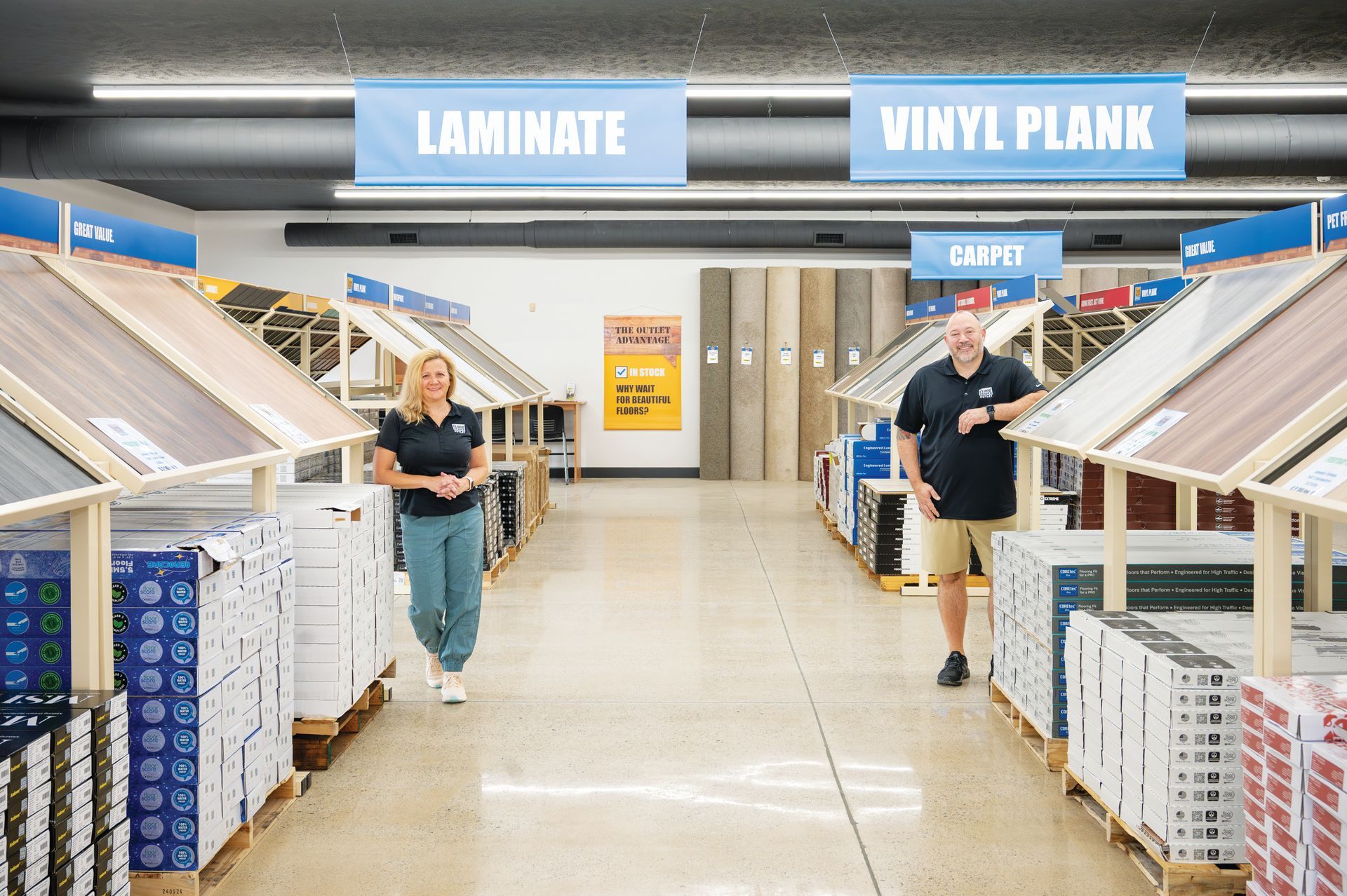 Two people stand in the aisle of a flooring store, surrounded by displays of laminate and vinyl plank flooring.