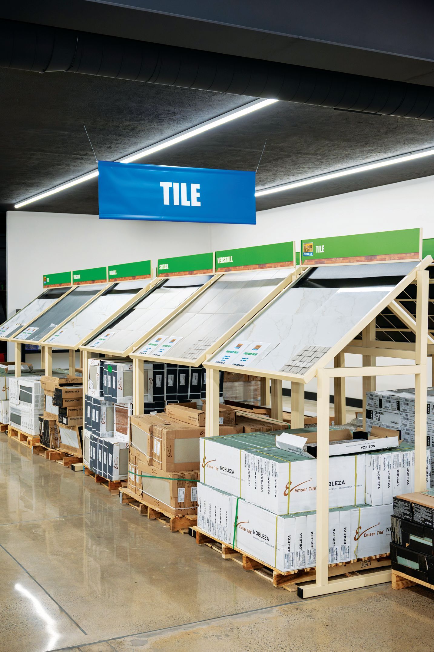 Rows of tile samples displayed on wooden shelving units under a blue 