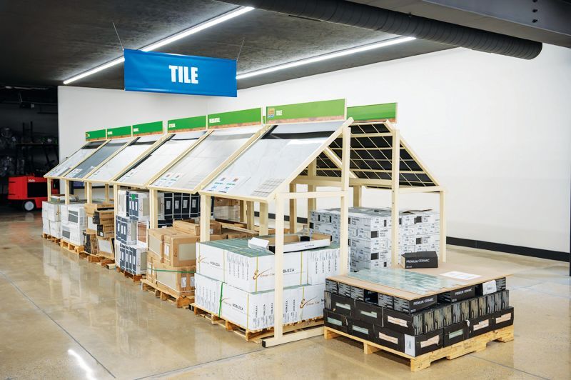 A tile display in a store, featuring wooden structures with sample roof tiles and palletized tile boxes on a concrete floor.