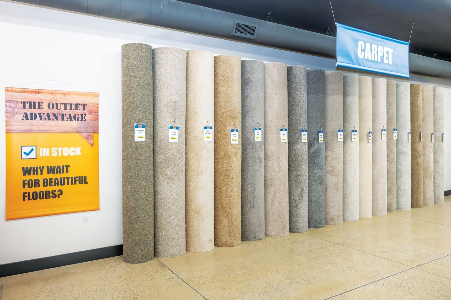 Rows of vertical carpet rolls in various neutral shades of beige, gray, and brown displayed in a flooring outlet.