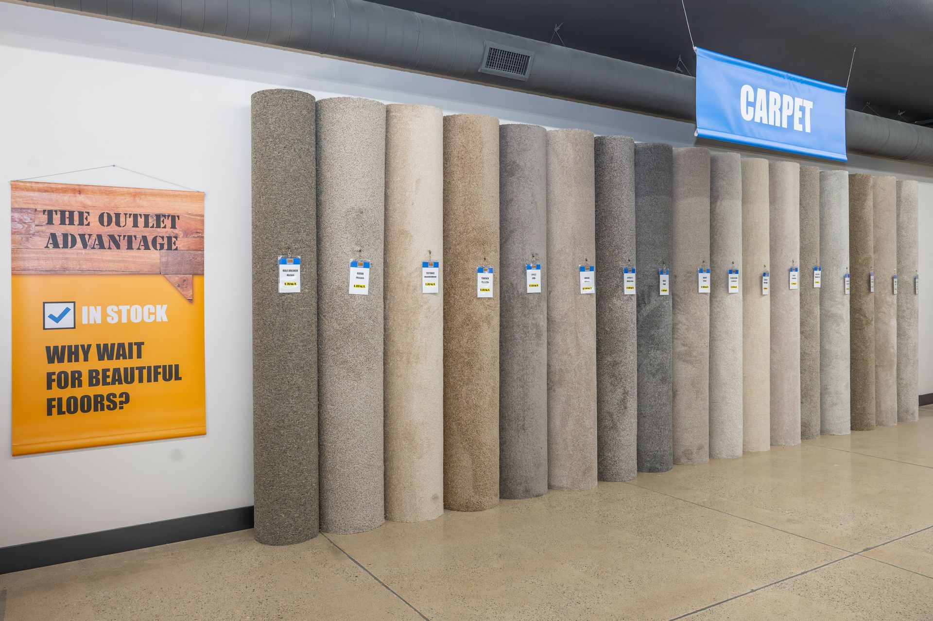 A row of carpet rolls in various neutral shades displayed in a store with a blue 