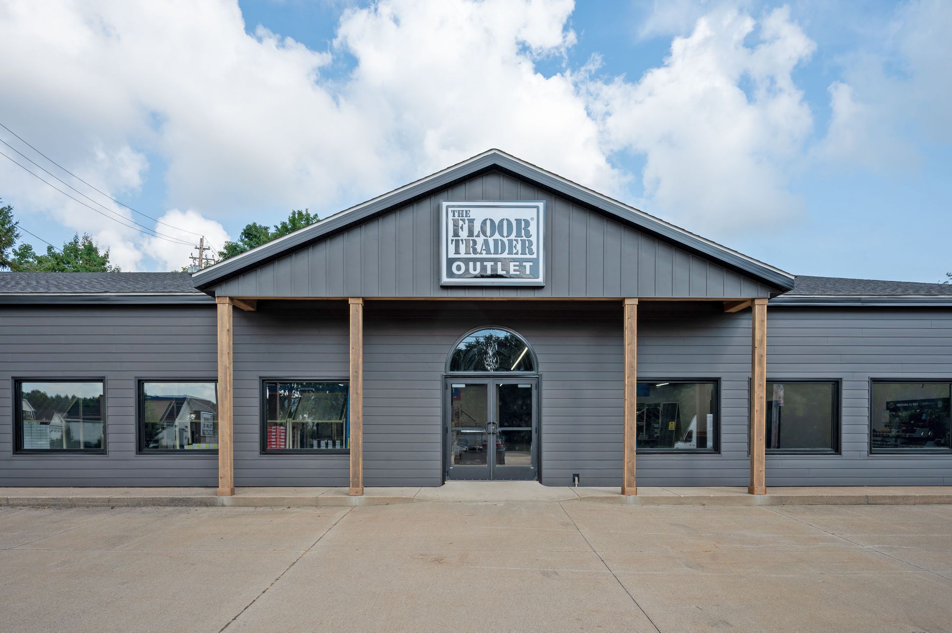 The exterior of a gray Floor Trader Outlet store featuring a centered arched entrance under a gabled roof.