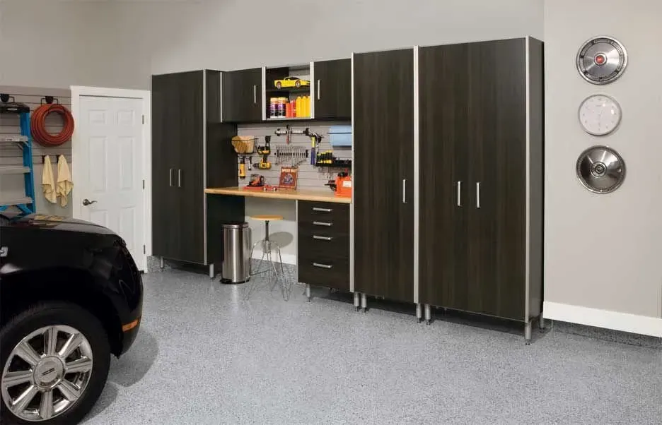 Garage storage system with dark wood-grain cabinets, a wooden workbench, and tools on a pegboard wall.