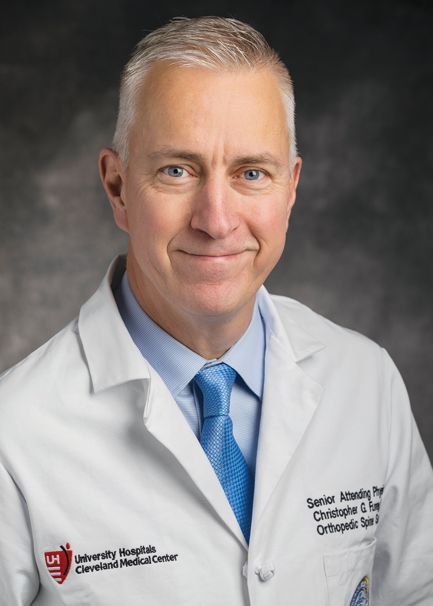 A professional headshot of an orthopaedic surgeon in a white lab coat with a University Hospitals medical center logo.